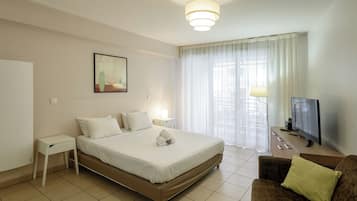 A hotel room with a large bed, a TV, a sofa, a bedside table, and a window with curtains.
