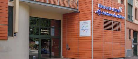 Eine Hotelansicht mit modernem Design, ausgestattet mit einem markanten Eingangsbereich mit Glastüren und einem Balkon darüber.