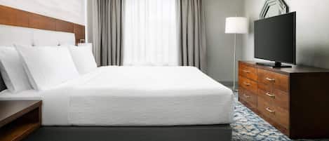 A hotel room with a large bed, a TV, a dresser, and a window with curtains.