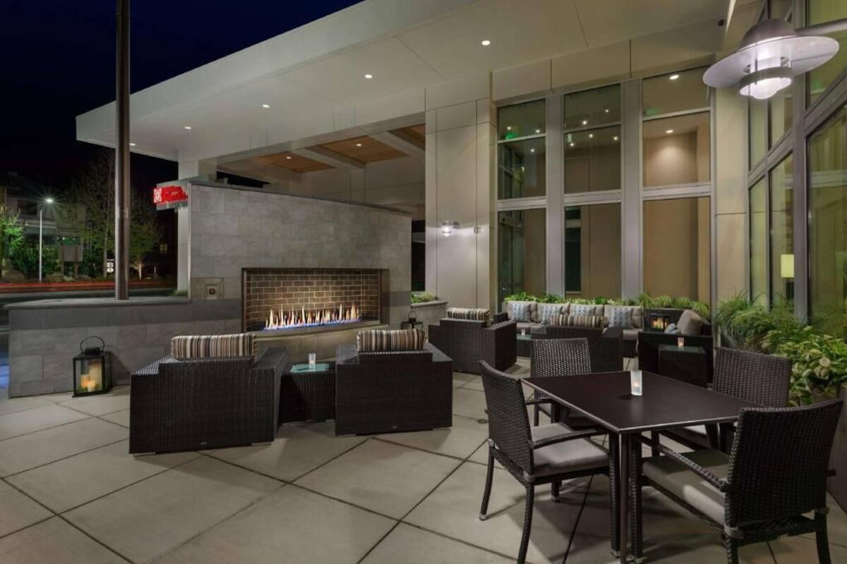 Een terras buiten met een bakstenen open haard, rieten meubels en een modern gevelontwerp.