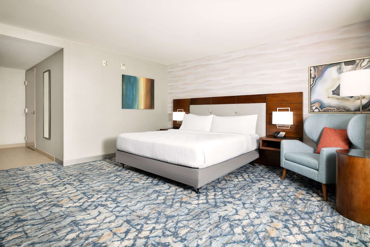 Een hotelkamer met een groot bed, een stoel, een nachtkastje en een schilderij aan de muur.