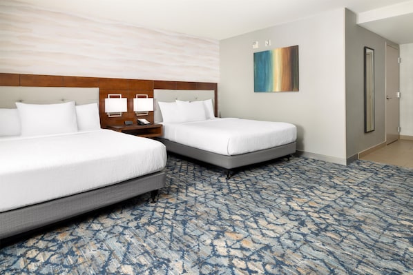 A hotel room with two beds, a nightstand, a painting, and a door.