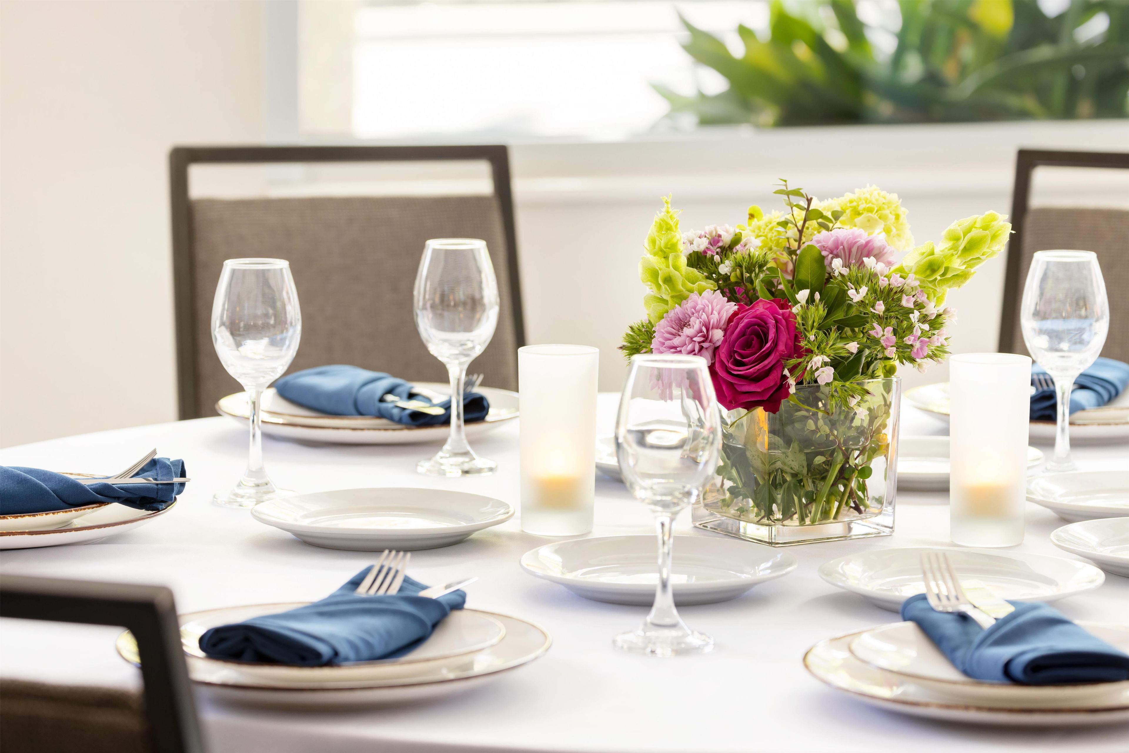 A dining table set for a meal with plates, cutlery, glasses, and a centerpiece of flowers.