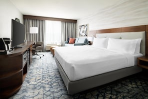 A hotel room with a large bed, a desk with a TV, a chair, a sofa, and a painting on the wall. - Hilton Garden Inn Palo Alto (Palo Alto)