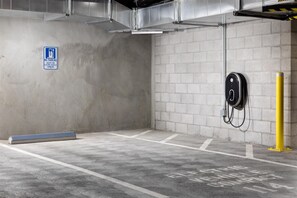 Un estacionamiento con paredes de concreto, un letrero de prohibido estacionar y estaciones de carga para vehículos eléctricos.