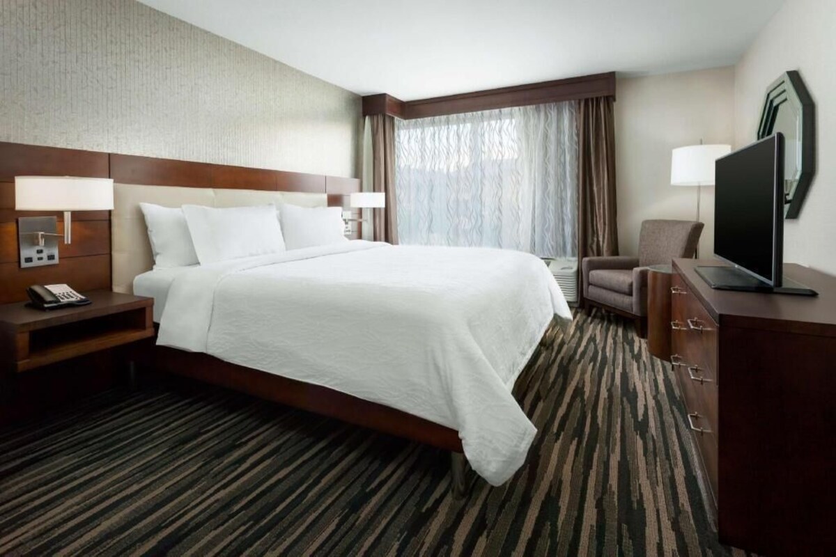 Habitación de hotel con una cama grande, un escritorio con teléfono, un televisor y una silla.
