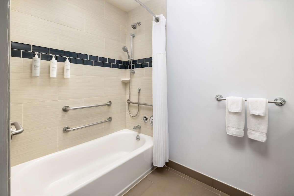 Een moderne badkamer met een bad, douche en handgrepen.