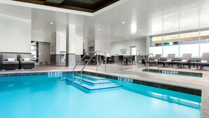 Een moderne binnenzwembadzone met duidelijke opgang naar het zwembad, comfortabele ligbedden en een ruime zithoek.