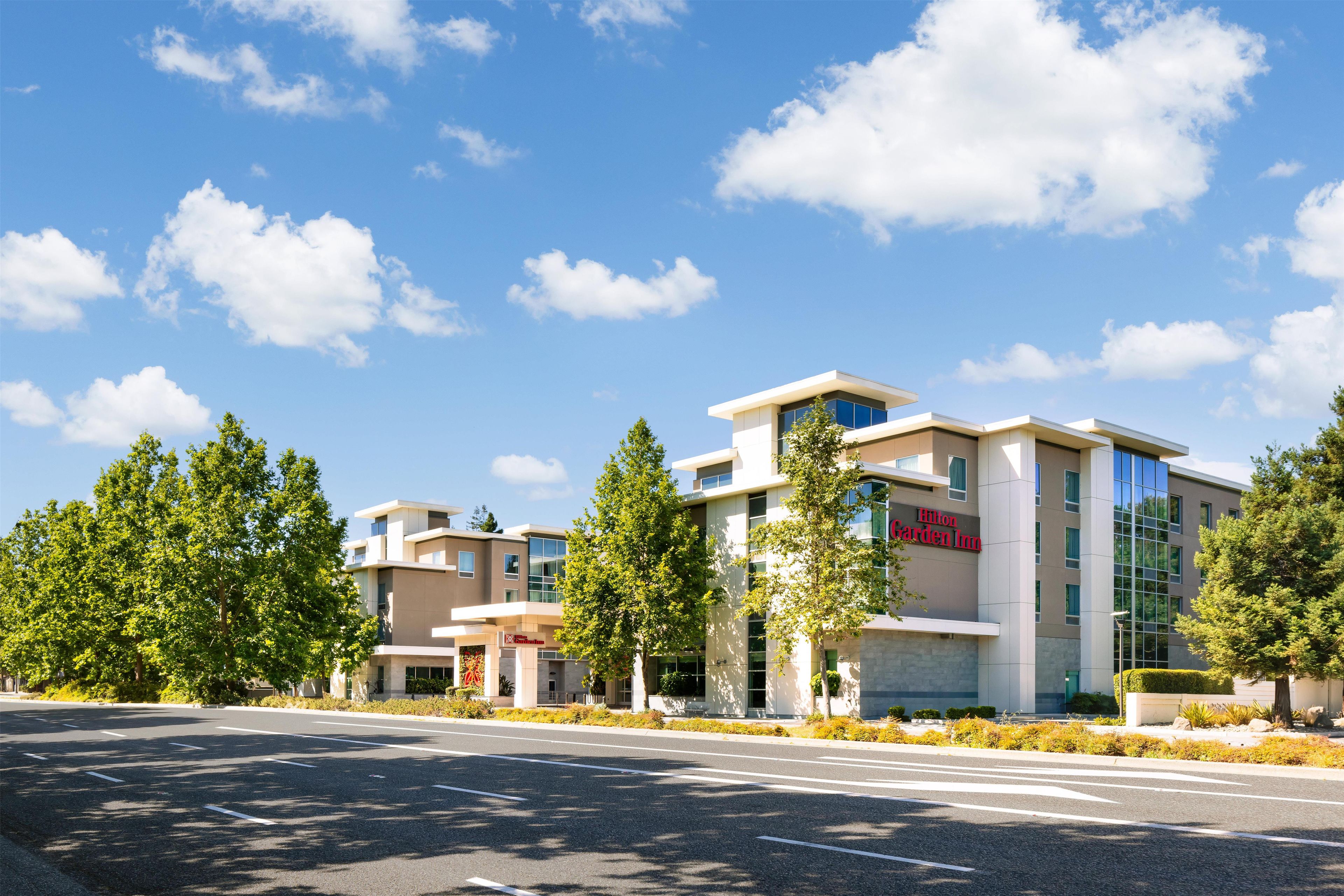 A modern hotel with a clear sky, a well-maintained lawn, and a road in the foreground.