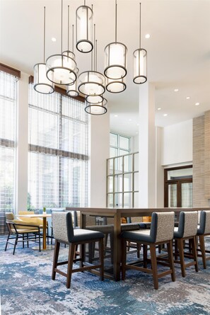 A modern dining area with a large wooden table, multiple chairs, and pendant lighting. - Hilton Garden Inn Palo Alto (Palo Alto)