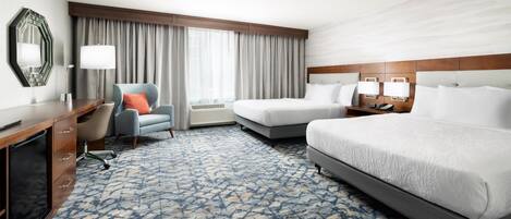 A hotel room with a large bed, a smaller bed, a desk with a chair, a TV, and a window with curtains.