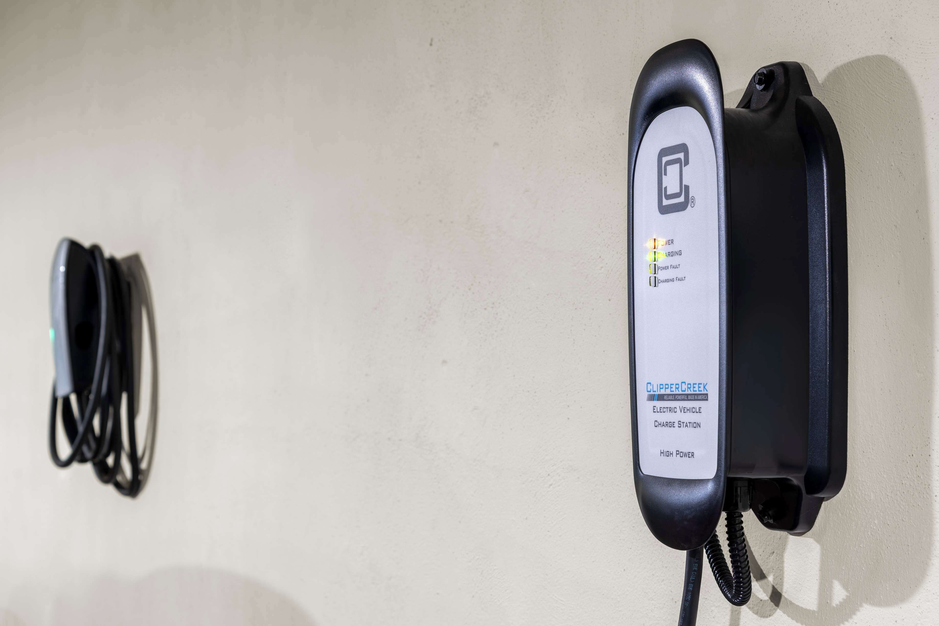 Une borne de recharge pour véhicules électriques fixée au mur, avec un câble enroulé à côté.
