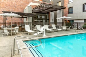 A poolside area with lounge chairs and umbrellas, a brick building in the background, and a clear blue pool. - Homewood Suites by Hilton Palo Alto (Palo Alto)