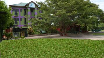 Un hotel con fachada verde y morada, césped cuidado y mobiliario exterior.