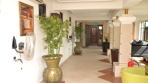 A hotel lobby with a tiled floor, potted plants, a reception desk, and a fire extinguisher. - Kaysens Grande Hotel (Tema)