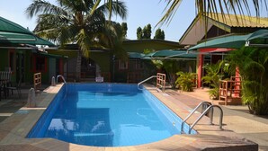 A swimming pool with a tiled edge, a wooden deck, and a palm tree. - Kaysens Grande Hotel (Tema)