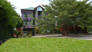 A building with a green and purple facade, surrounded by well-maintained grass and trees. - Kaysens Grande Hotel (Tema)