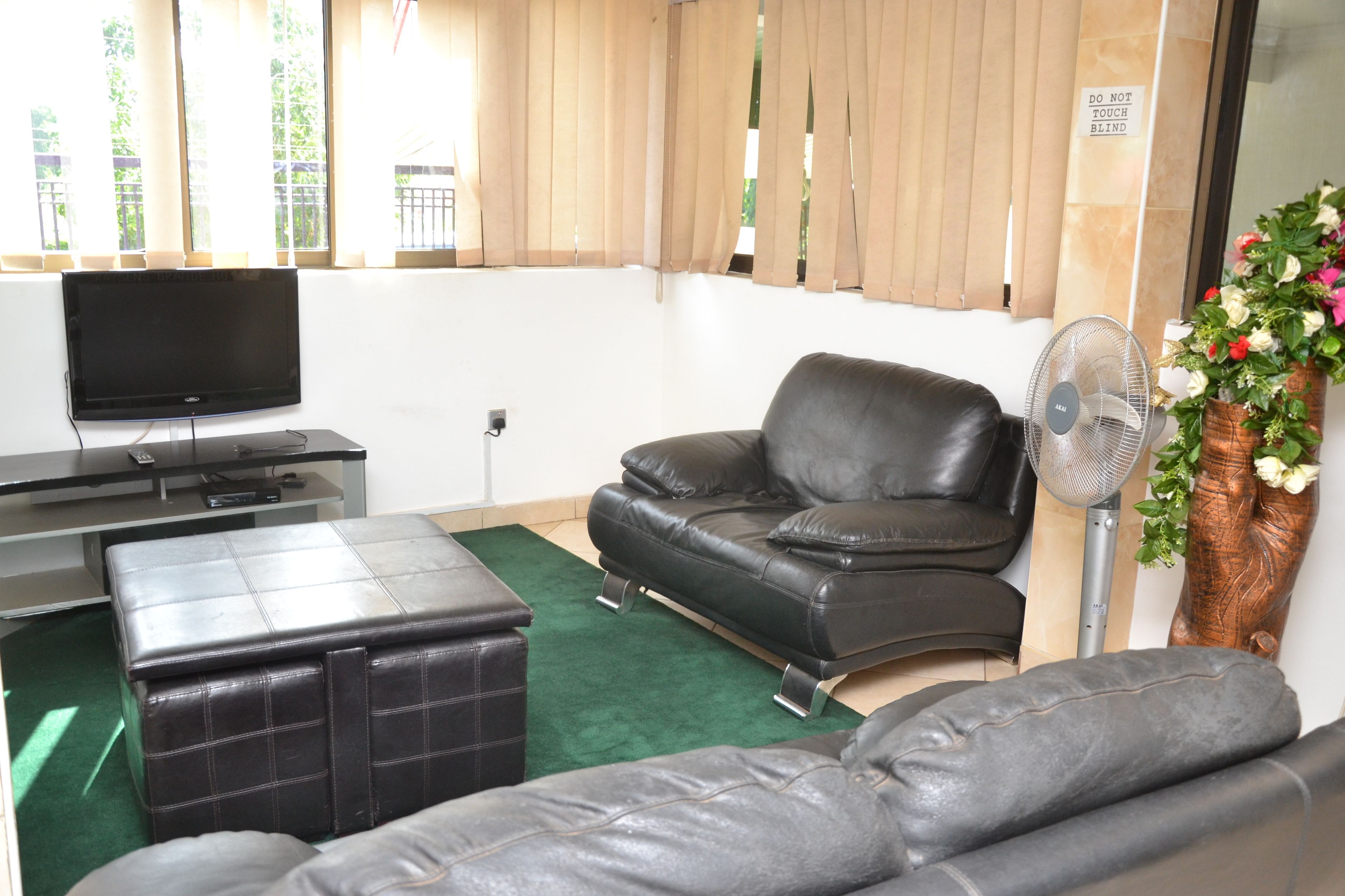 A living room with a black leather sofa, a matching ottoman, a flat-screen TV, and a wall-mounted fan.