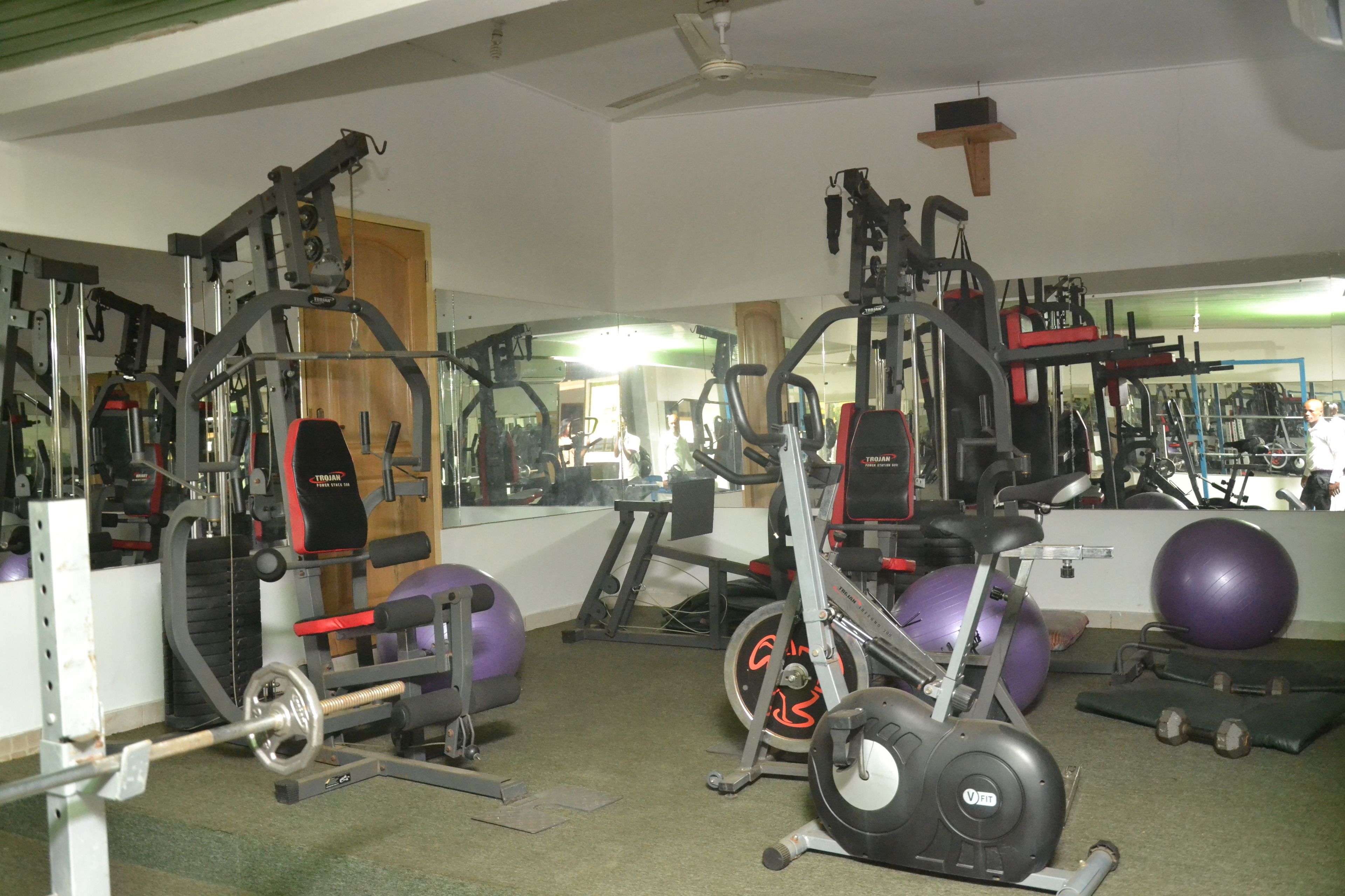 A gym with exercise equipment, mirrors, and a ceiling fan.