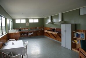 A compact kitchen with a dining table and chairs, a refrigerator, and a bookshelf. - Cottage Park Motor Lodge and Conference Centre (Otaki)