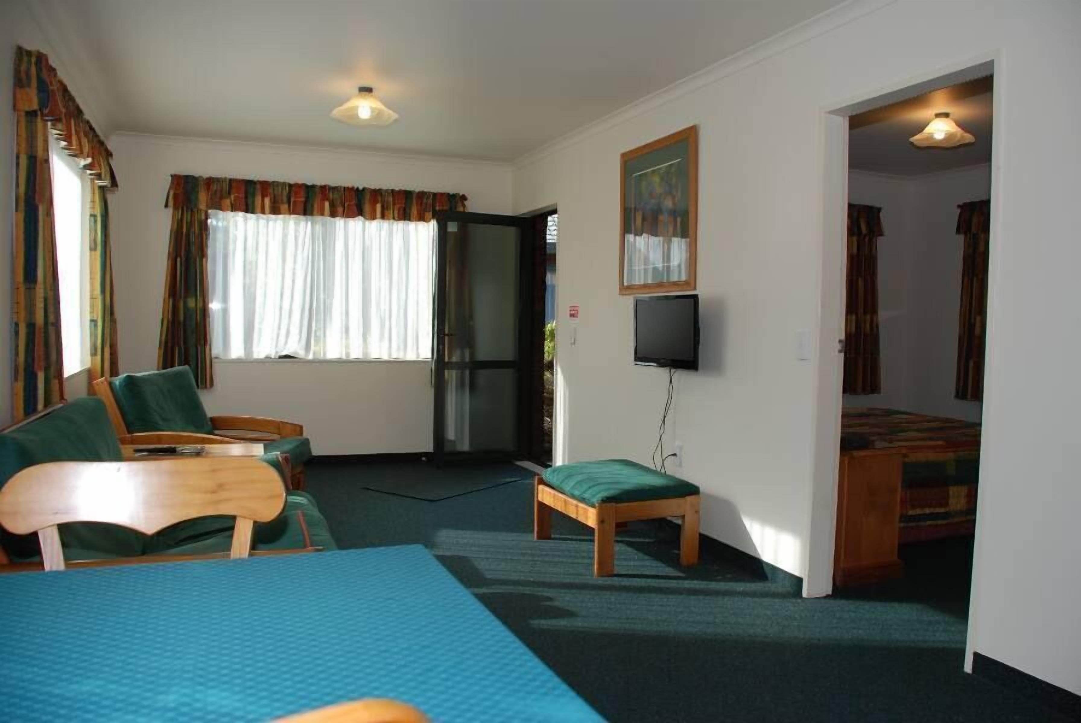 A room with a bed, a desk, a chair, a television, and a window with curtains.
