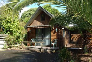 A wooden cabin with a porch, two chairs, and a bench. - Cottage Park Motor Lodge and Conference Centre (Otaki)
