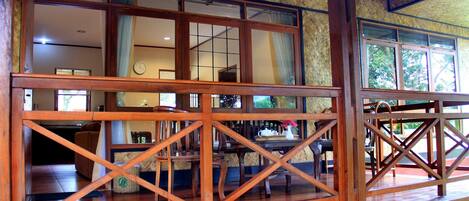 A wooden balcony with a view of the interior, including a dining area and a clock on the wall.