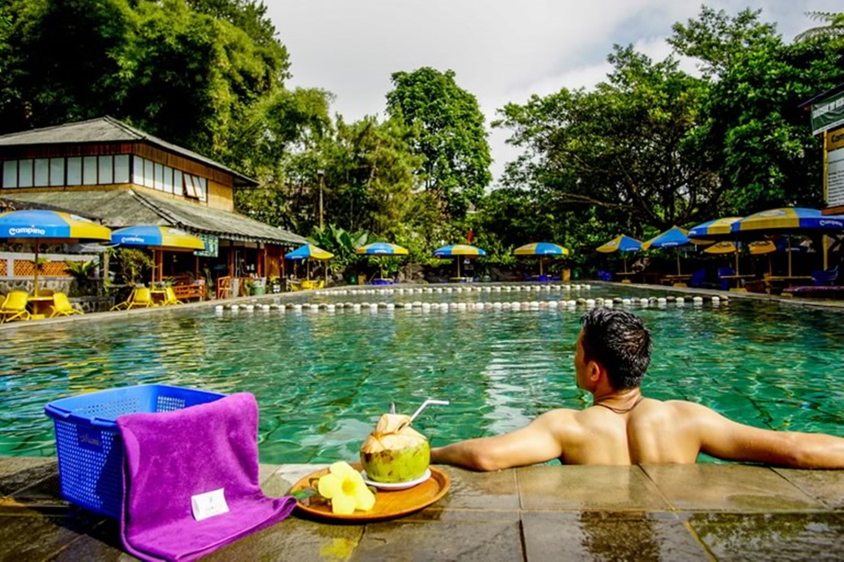 A man relaxing in a swimming pool with a drink and a towel nearby.