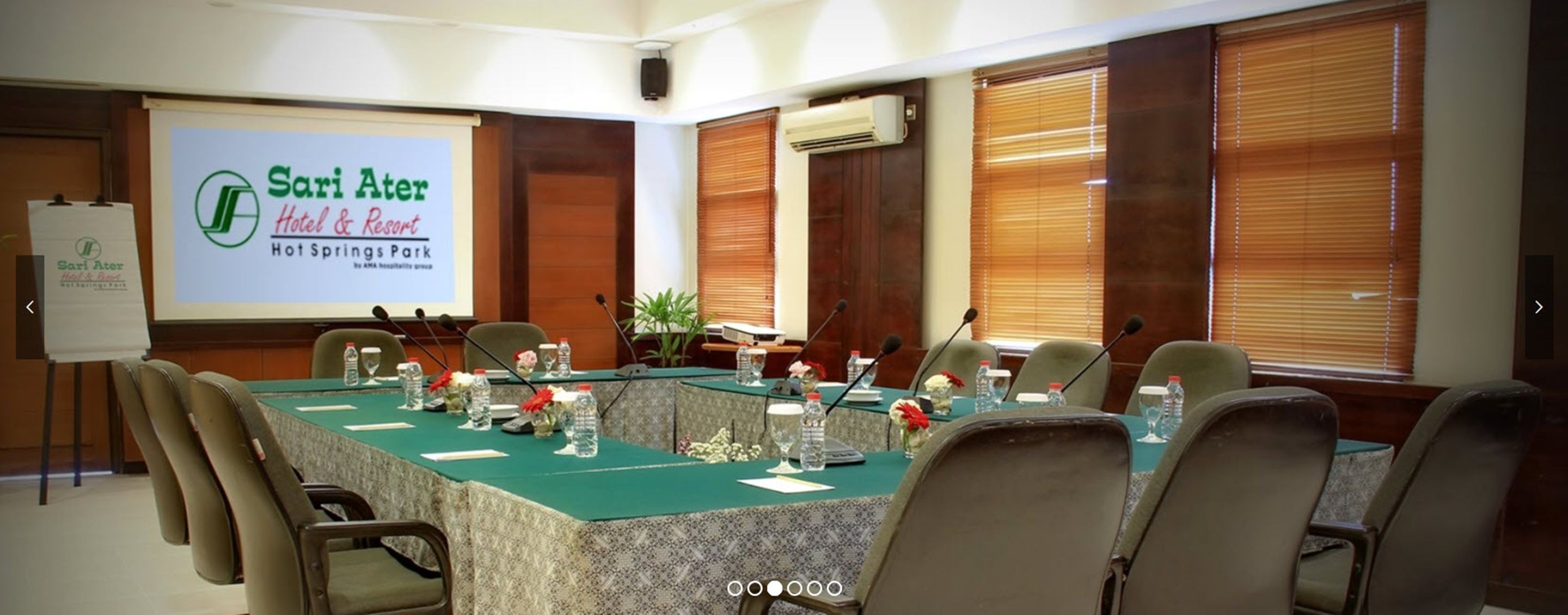 A conference room at Sari Ater Hotel & Resort with a large screen displaying the hotel's name, a long table with chairs, and a whiteboard.
