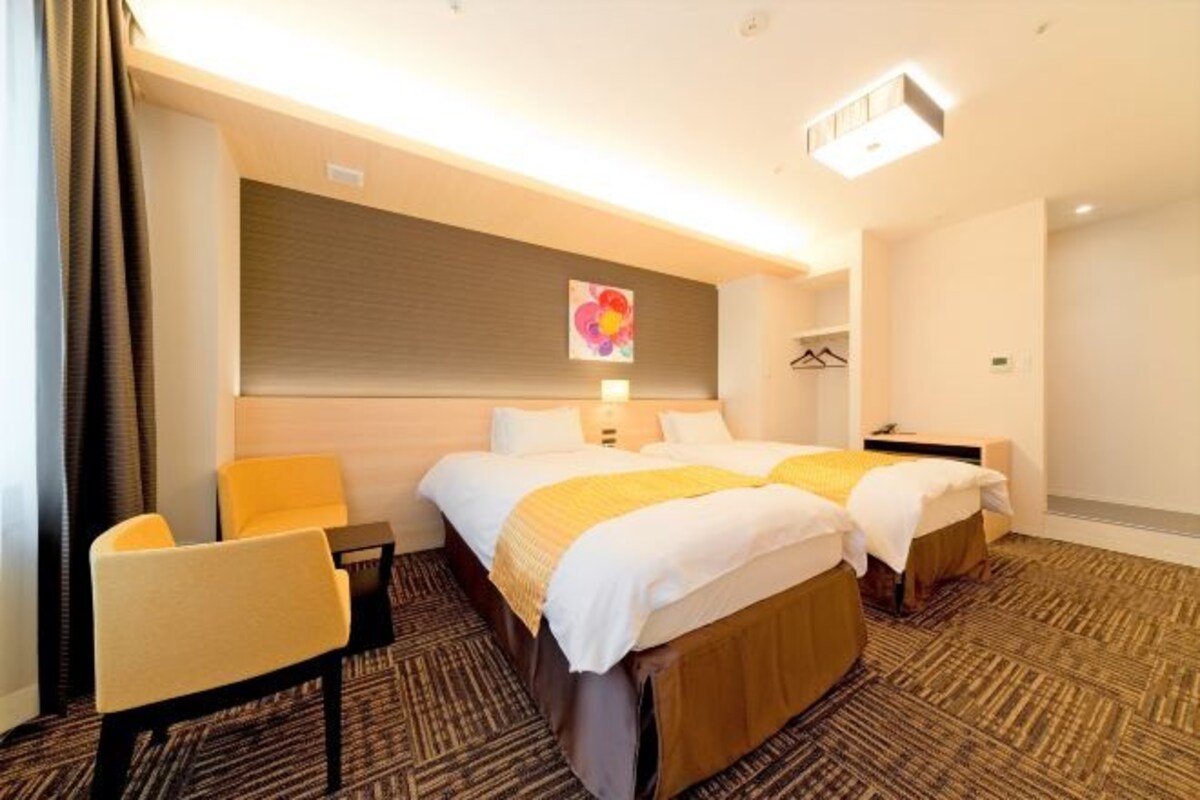 A hotel room with two beds, a chair, a desk, and a coat rack.