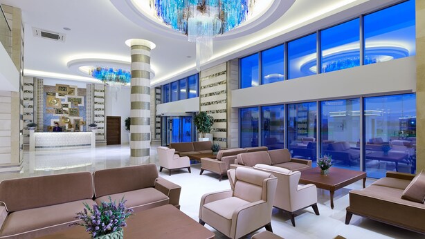 A spacious lobby with modern furniture, a large chandelier, and large windows offering a city view.