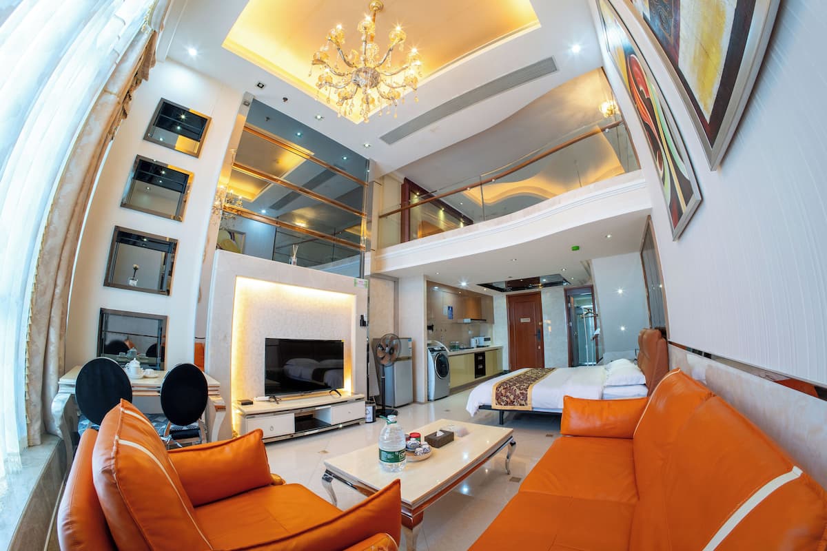 A modern hotel room with a dining area, a kitchen, and a living space with orange furniture.