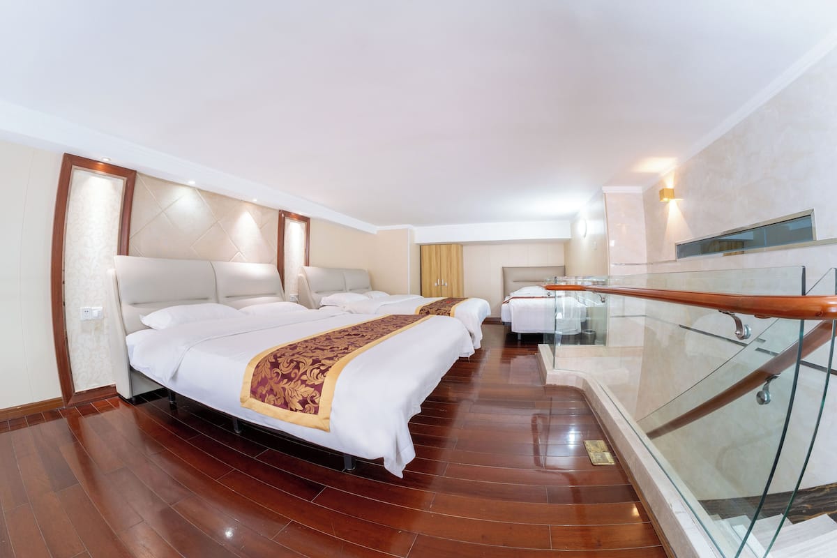 A hotel room with a large bed, a smaller bed, a glass railing, and a wooden floor.