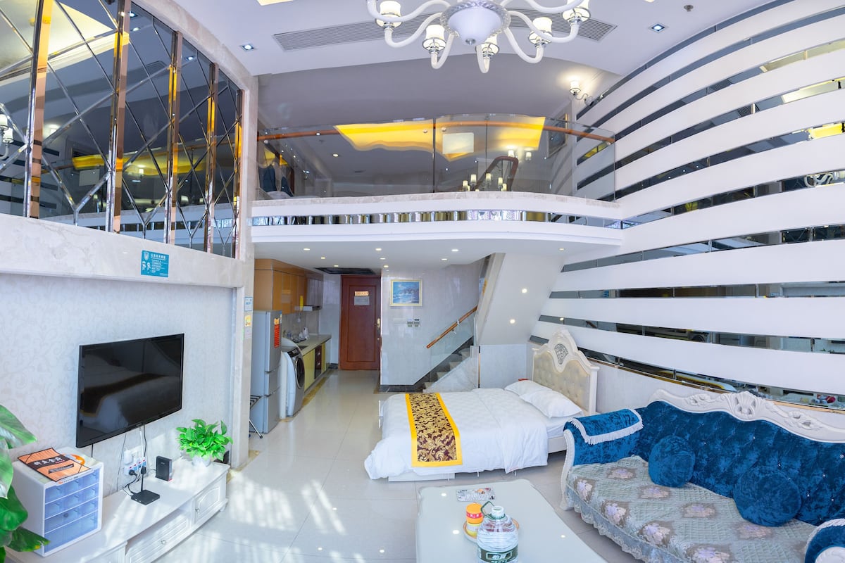 A modern hotel interior with a spacious living area, a flat-screen TV, a sofa, a bed, and a staircase leading to an upper level.