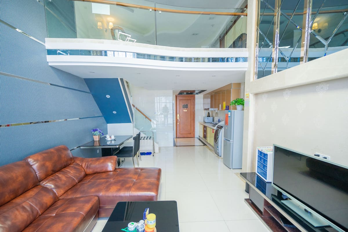 A modern living room with a leather sofa, a flat-screen TV, and a dining area with a table and chairs.