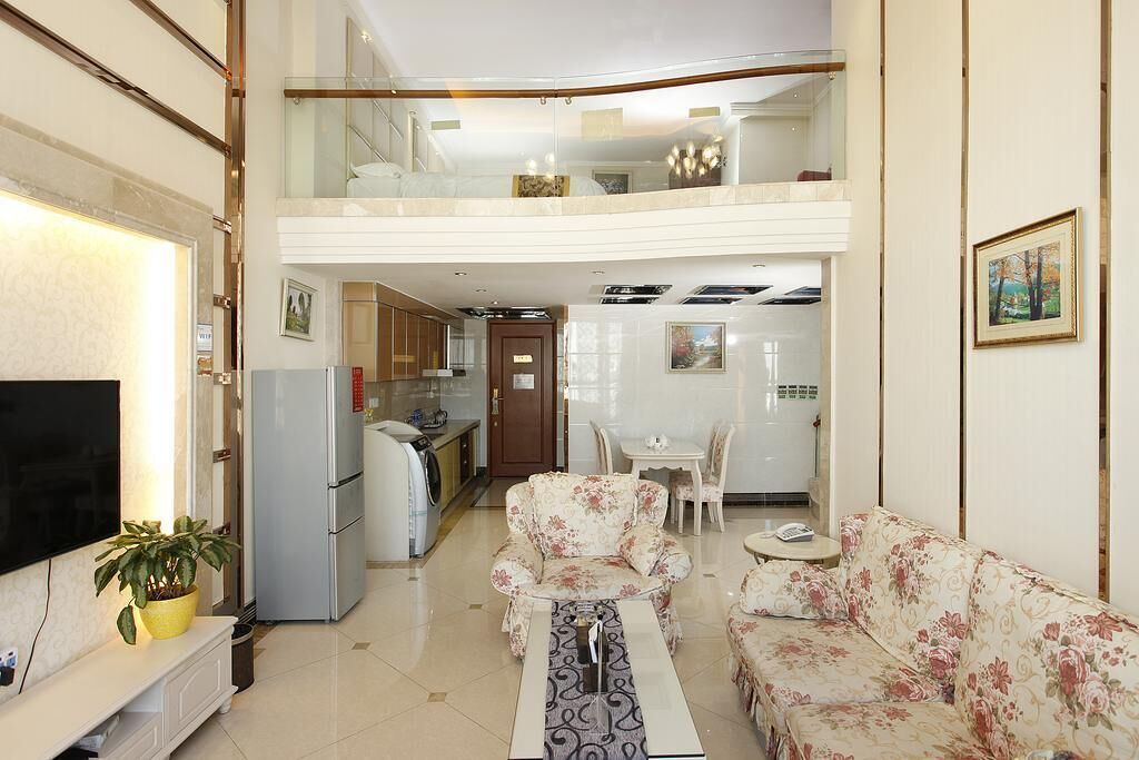 Ampla sala de estar com sofá, mesa de centro, televisão e cozinha ao fundo.