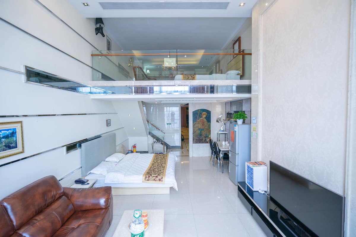 A modern hotel room with a balcony, a sofa, a TV, and a dining area with chairs and a table.