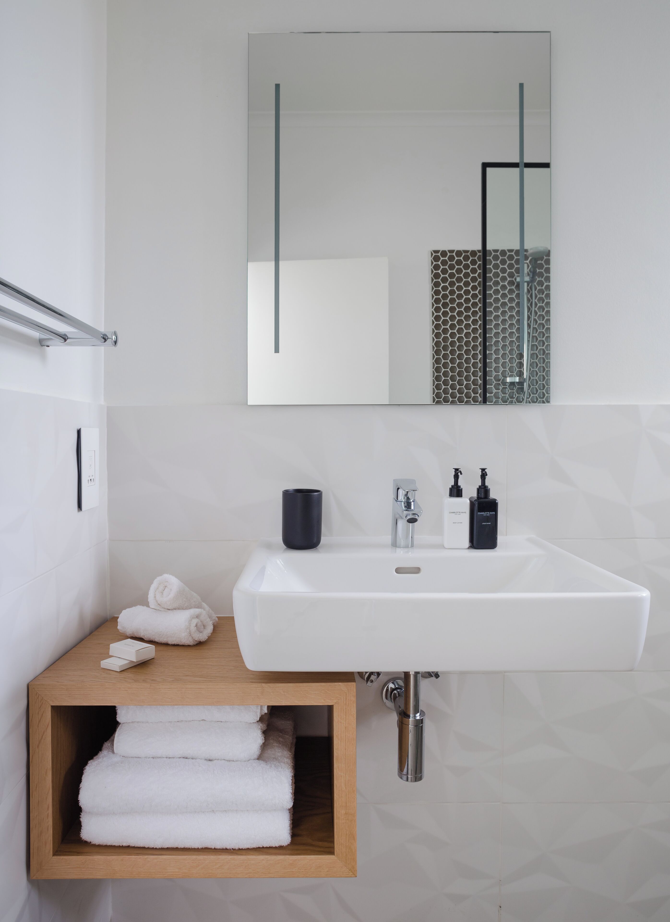 A bathroom with a white sink, a mirror, a towel rack, and a wooden shelf with towels.