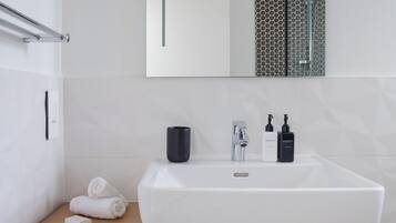 A bathroom with a white sink, a mirror, a towel rack, and a wooden shelf with towels.