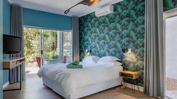 Quarto moderno com uma cama grande, televisão e vista do jardim pela porta de vidro.