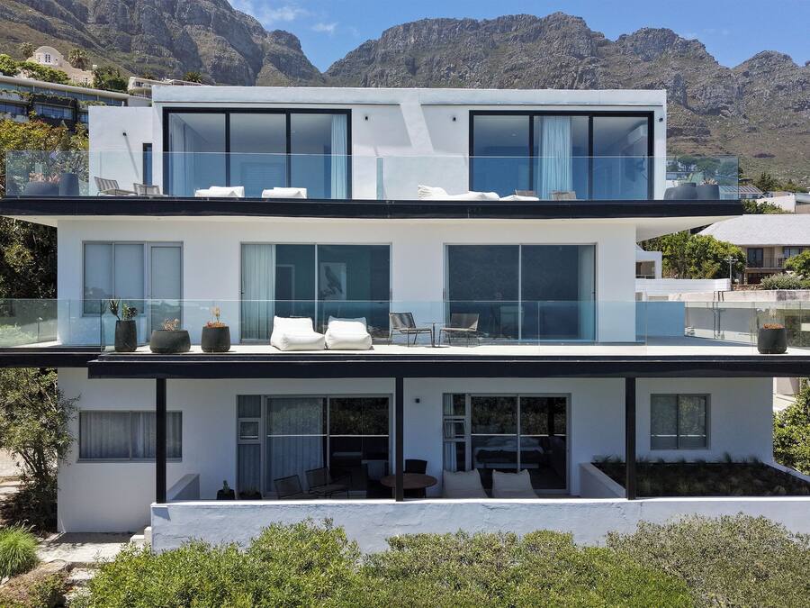 Un edificio moderno de dos pisos con grandes ventanales, asientos al aire libre y vista a las montañas.
