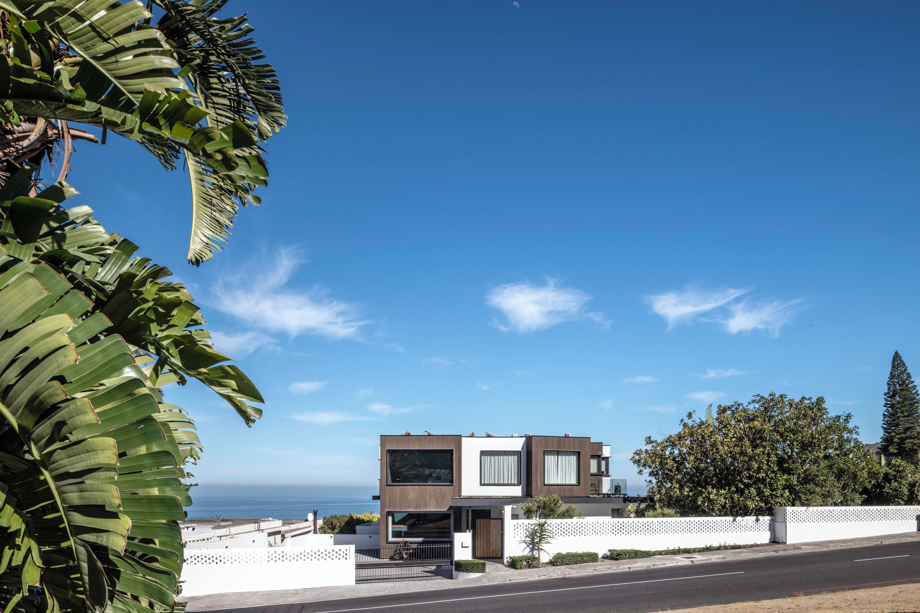 A modern two-story house with a garage, white fence, and a view of the ocean.