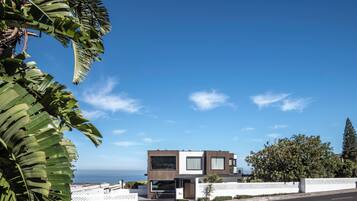 A modern two-story house with a garage, white fence, and a view of the ocean.
