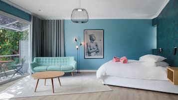 A modern bedroom with a teal wall, a white bed, a green sofa, and a wooden coffee table.