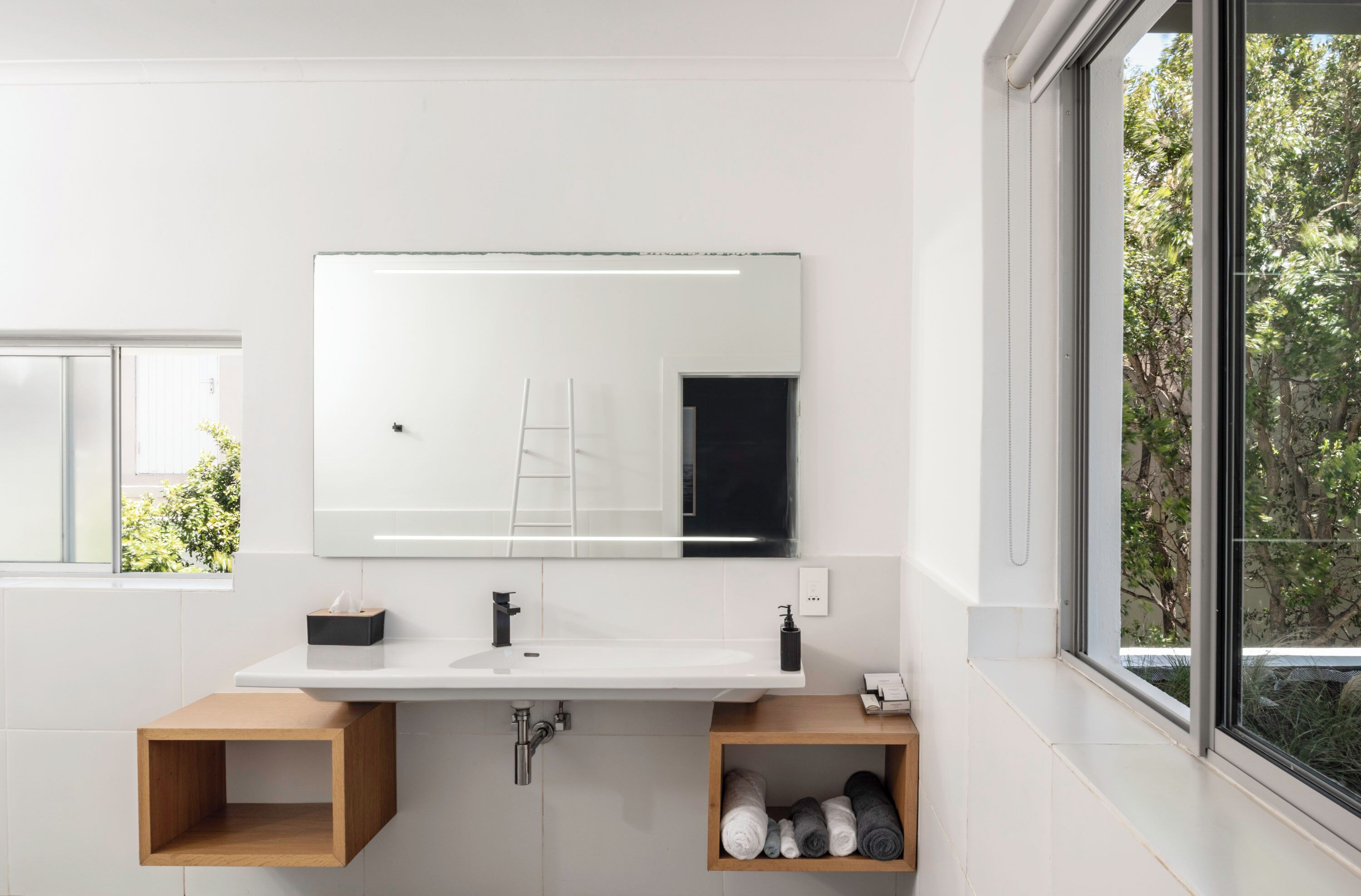 Un baño moderno con lavamanos blanco, espejo y estantes de madera.