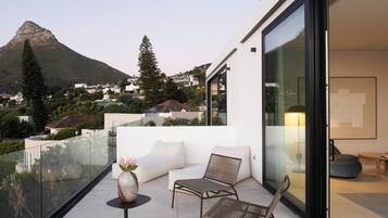 A modern balcony with a glass railing, a sofa, a chair, and a table with a vase.