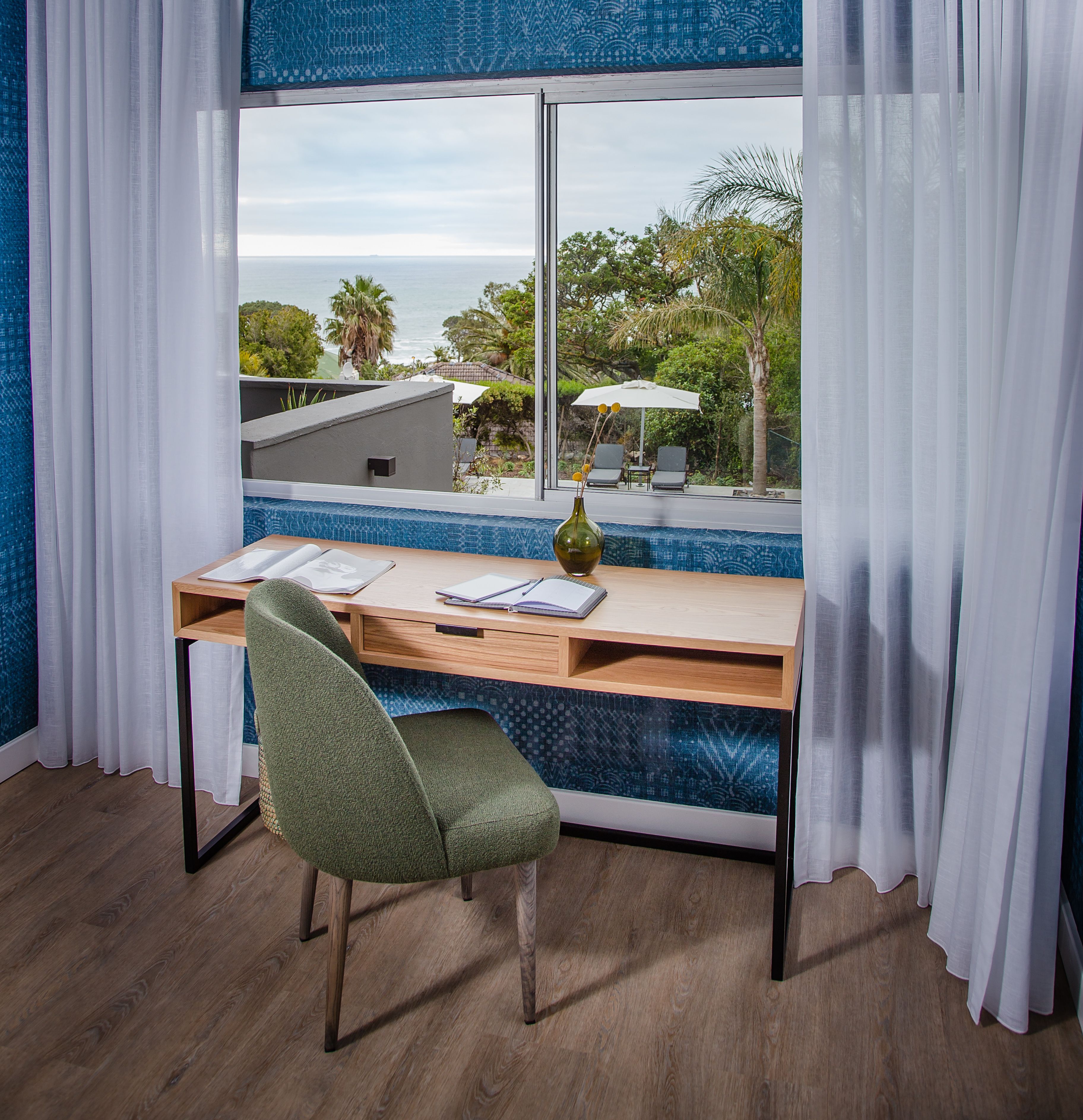 A room with a desk, chair, and a view of a swimming pool and greenery.