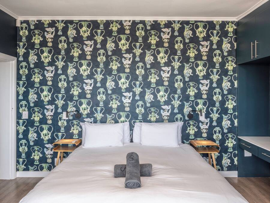 A bedroom with a large bed, two bedside tables, and a dark patterned wallpaper.