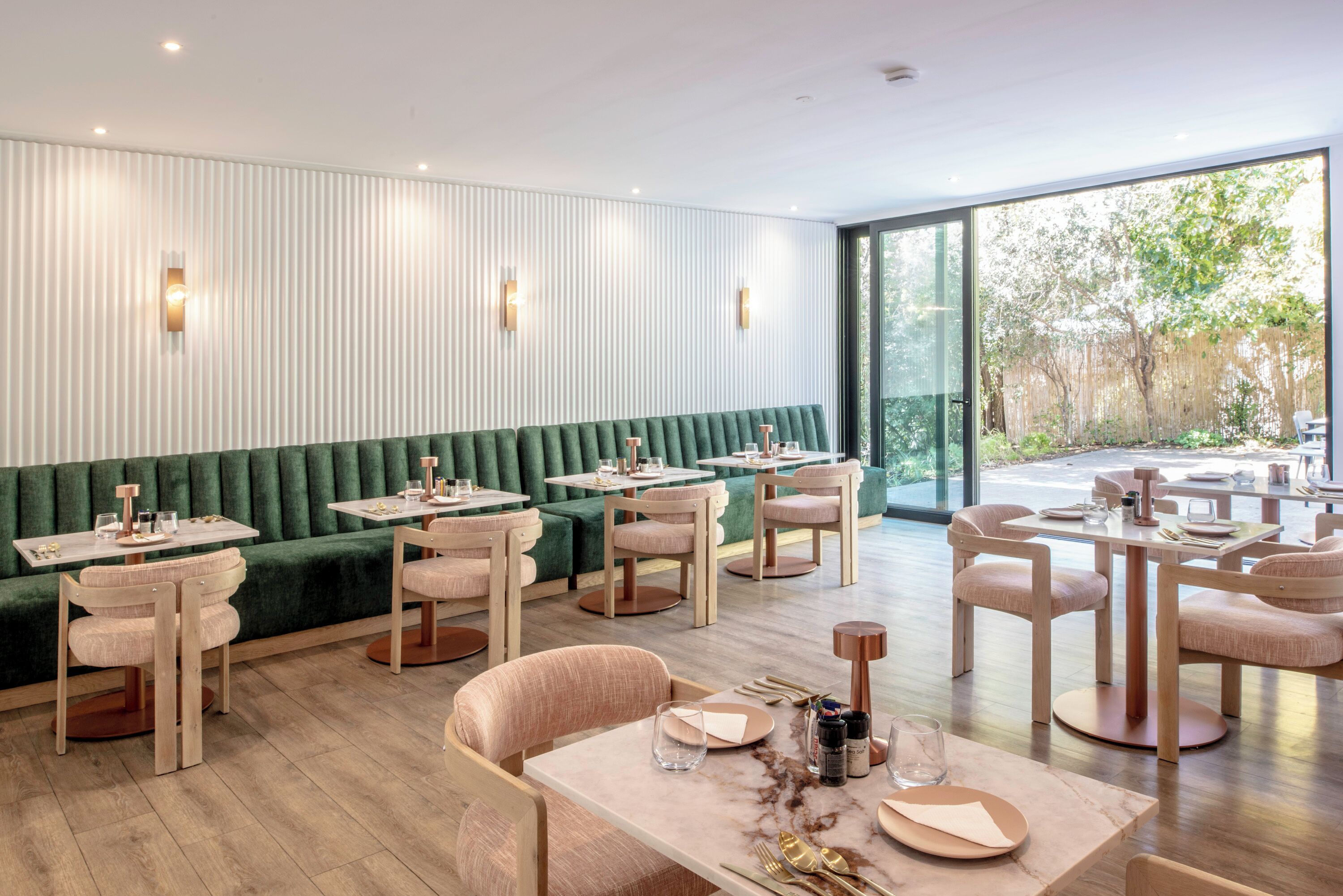 A modern restaurant with green upholstered seating, wooden tables, and light fixtures.