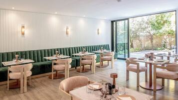 A modern restaurant with green upholstered seating, wooden tables, and light fixtures.